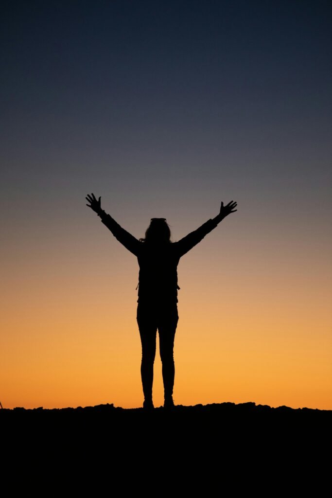 A silhouette of a person standing with arms raised against a vibrant sunset sky.