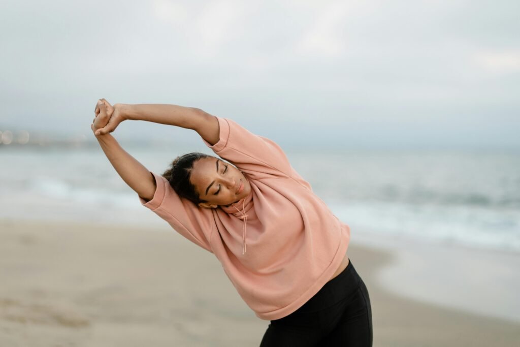 A woman performs a side stretch by the ocean, promoting wellness and relaxation.